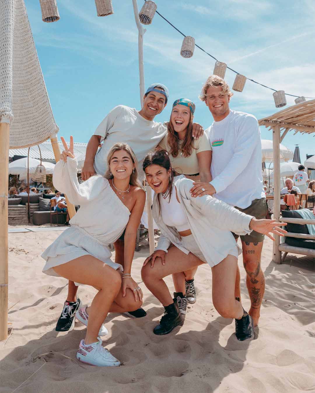 Groep personeel lachend naar de camera in het zand met blauwe lucht