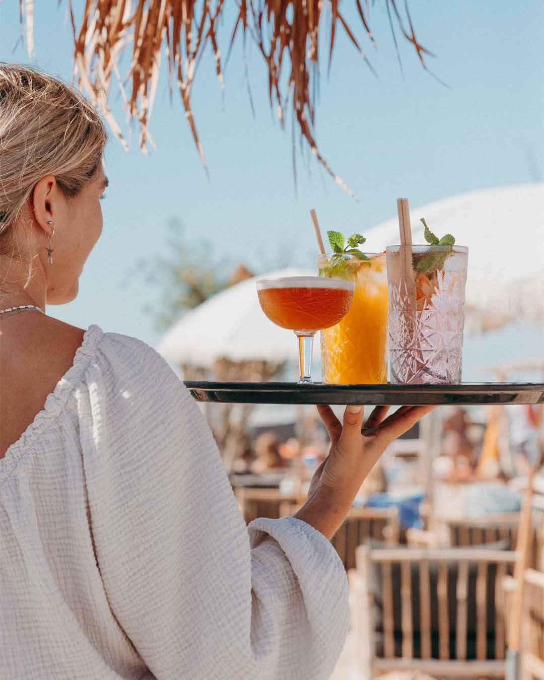 Meisje met verschillende cocktails op dienblad onder zonnige lucht