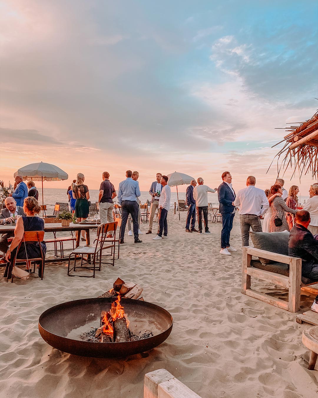 Mensen op een bruiloft in het zand bij ondergaande zon voor vuurschaal